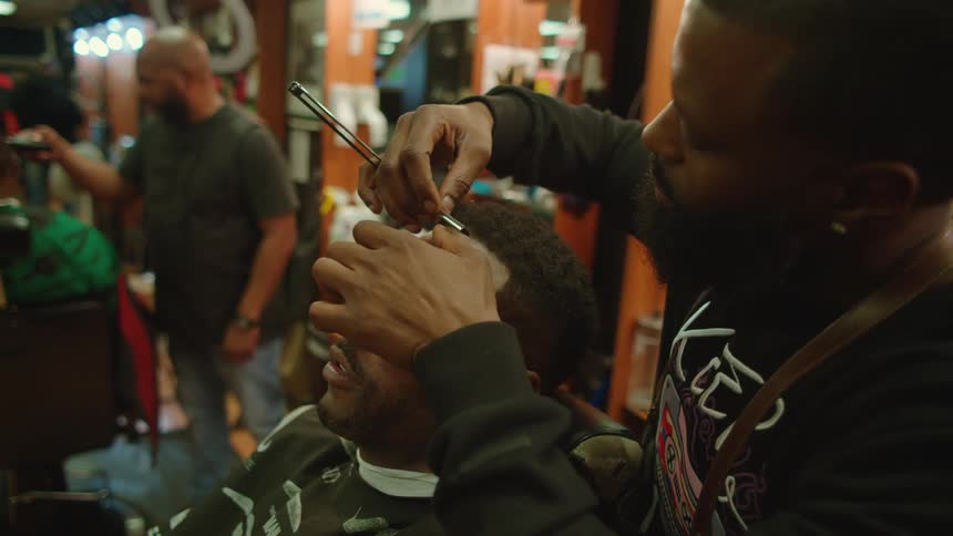 A barber uses a razor to shape the hairline of a customer in a barber shop