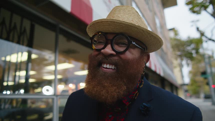 A man is standing outdoors by a store and is smiling