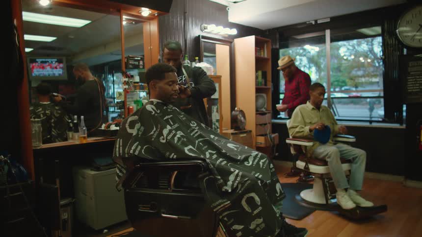 Two men are getting haircuts at a barber shop during the day