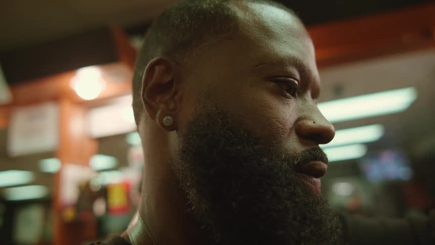 Barber with earring and long beard shaves customer in barber shop