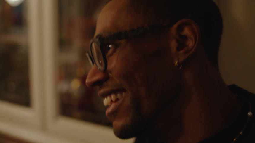 Man wearing eyeglasses smiles and laughs as he talks with glass fronted cabinet in background