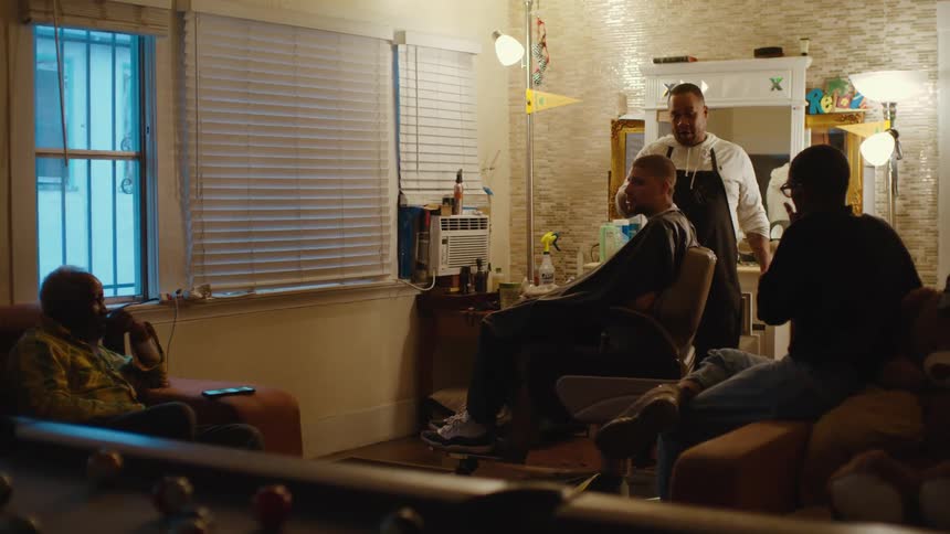 Men sit and watch as barber and his customer talk to each other