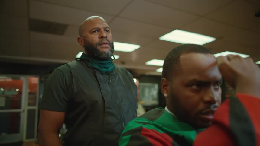A man points to his beard and hair as he tells a barber what he would like done