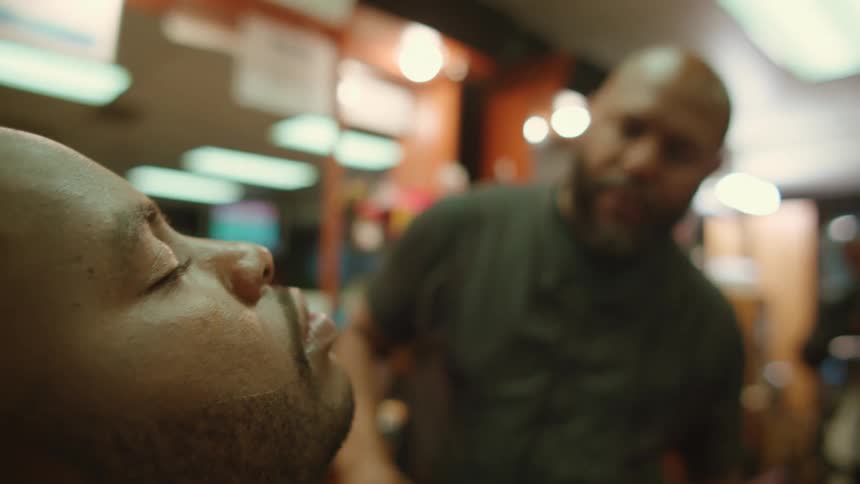 Bold barber with beard and black t shirt with vest shaves mans beard with straight razor in barber shop