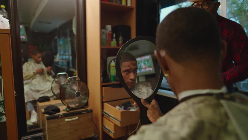Barber stands watching client check his hair in a hand mirror