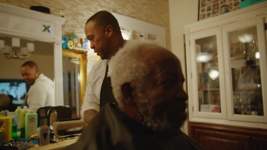 A black male barber is preparing a customer for a hair cut