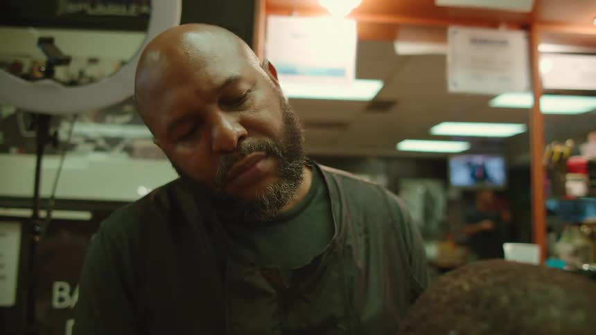 Bald barber with beard black t shirt and vest cuts mans hair with scissors in barber shop