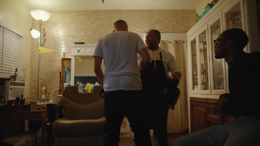 A barber takes a cape off a man and then they hug and the man gives the barber money and they bump fists