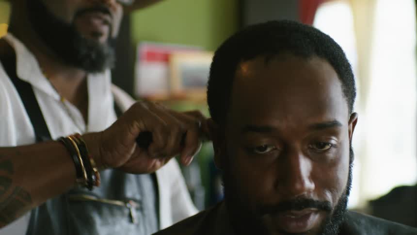 Barber combs mans hair as the man views mobile phone