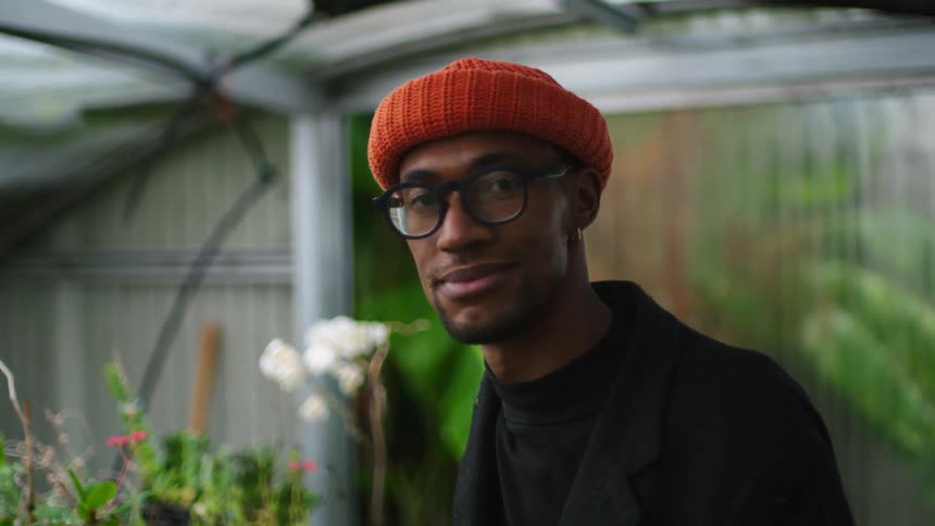 A man smiles as he poses near plants in a greenhouse