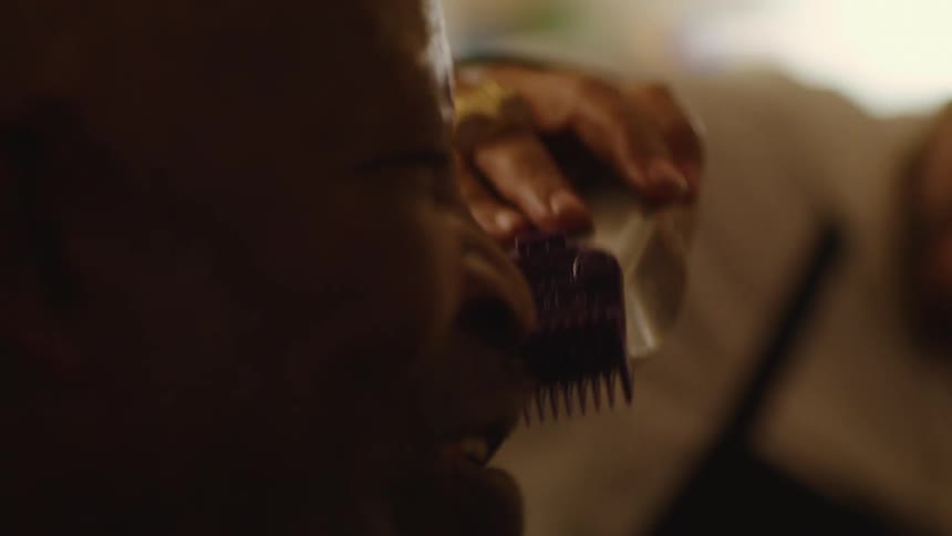 Barber with white shirt and black apron shaves middle aged man with clippers in barber shop
