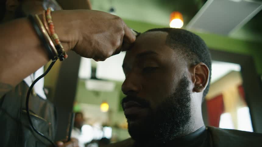 Barber gives a haircut to a client with electric clippers inside a barber shop