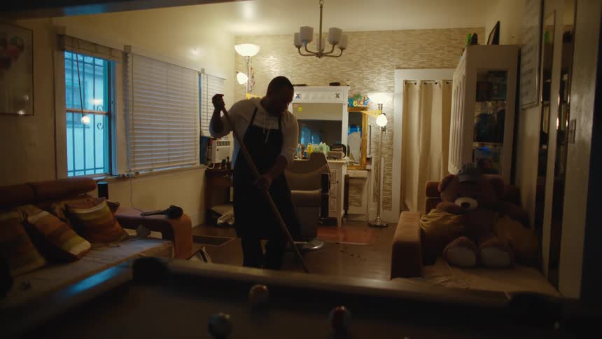 A man wearing an apron sweeps the floor around a barbers chair