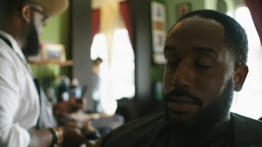Barber uses electric clippers on the back of the head of a client in the barber shop