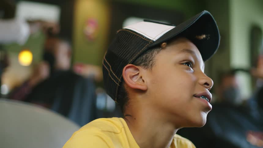 Boy with cap yellow t shirt and dental braces looks up and smiles in barber shop