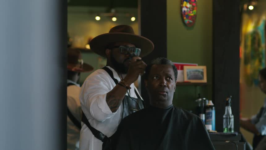 Barber with hat white shirt and black apron trims mans hair with clipper in barber shop