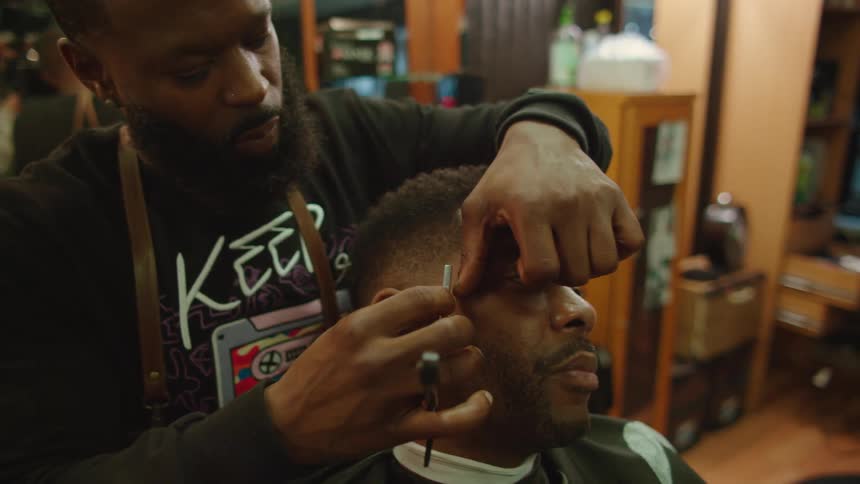Man with beard black sweater and beard shapes a mans hairline with a straight razor in barber shop