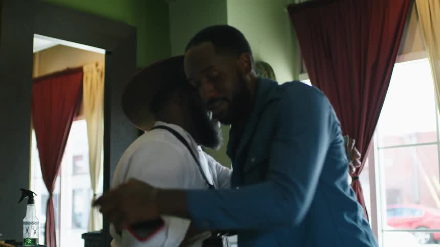 Customer pays man wearing hat then hugs him and shakes hands before leaving