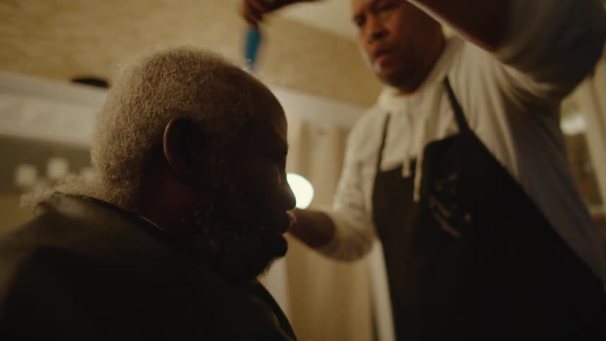 A barber clips a mans hair and then combs it