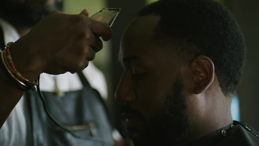 A man talks with his barber while having his hair cut in a barber shop during the day