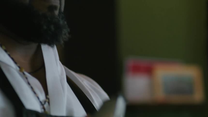 Male barber with hat glasses beard white shirt and black apron cuts mans hair in barbers shop