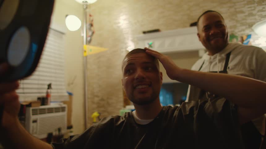 A man is looking at his new haircut and using a mirror