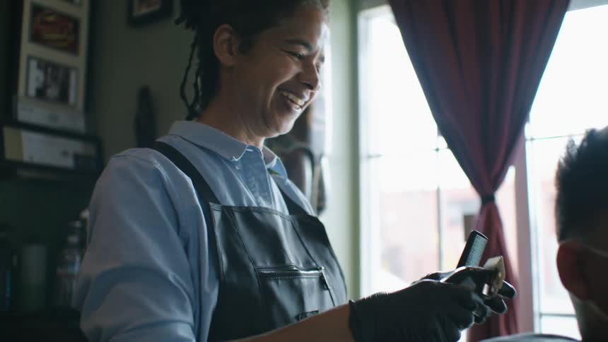 Hairstylist smiles while cutting clients hair with electric clippers