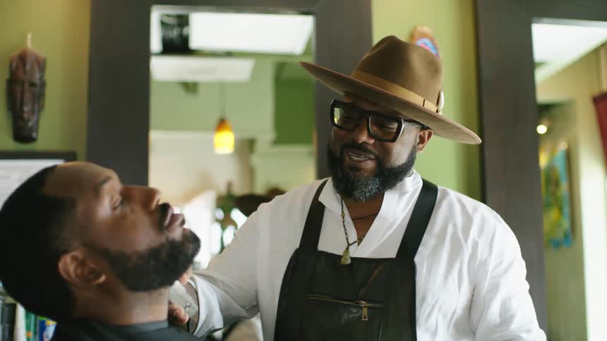 Barber shaving the beard of a client with an electric trimmer in the barber shop