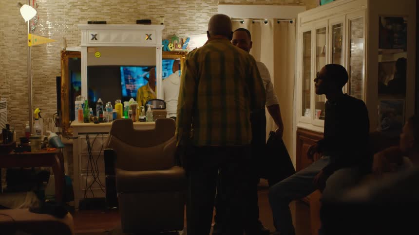 A man turns and shakes the barbers hand while other men sit and talk
