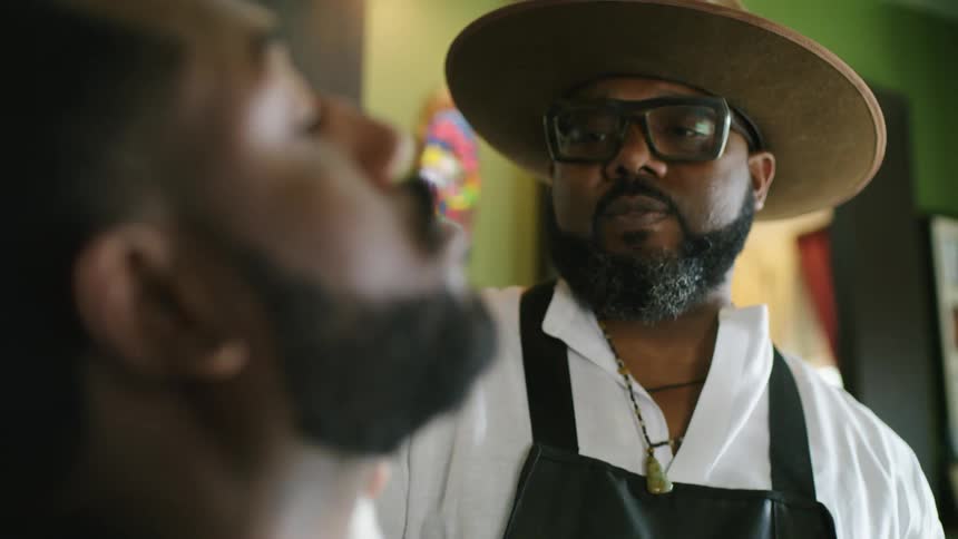 A barber talks to a customer as he shaves his beard