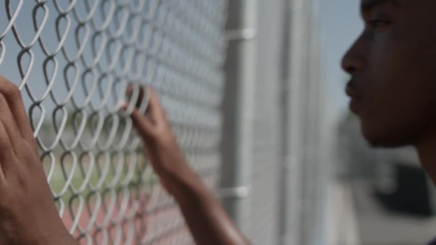 A boy is leaning against a fence of a field