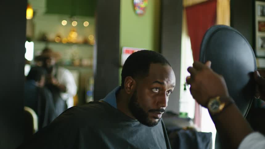Barber holds up mirror for customer to check out the trim