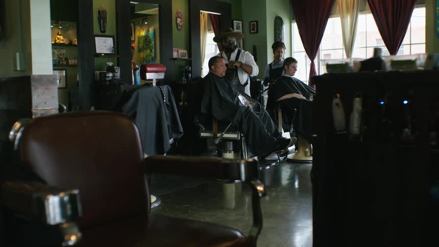 Two customers are getting their hair cut at a barber shop