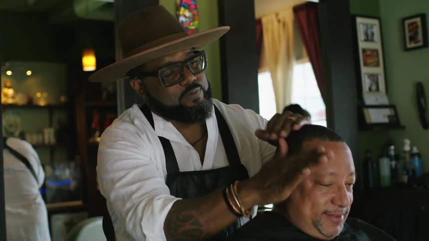 Barber rubbing lotion on the head of a client sitting on a chair inside a barber shop