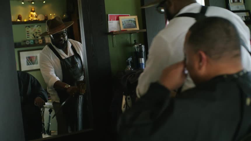 A male barber brushes off loose hairs on the back of a clients neck in a salon