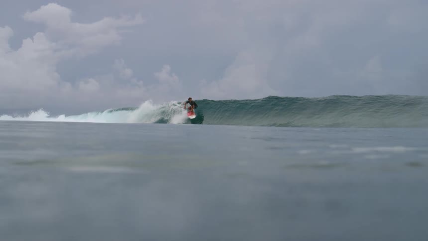 Surfer uses a red and white surf board to ride a wave on the ocean