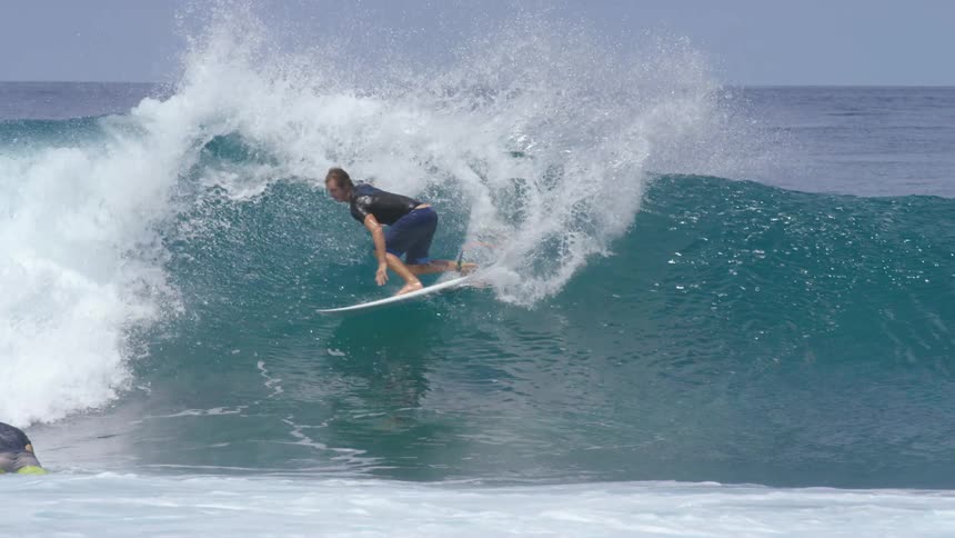 Surfer rides board over wave as another man paddles on his board