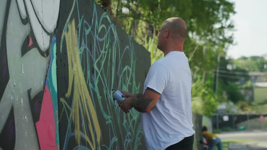 A man is spray painting a wall outdoors in spring