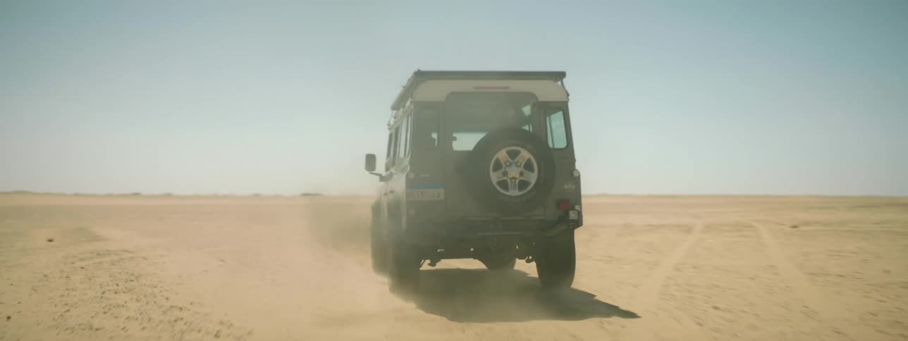 A man drives a jeep across a desert flatland during the day