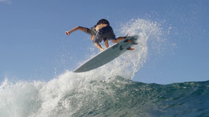 Young man rides a white surfboard over an ocean wave under a blue sky