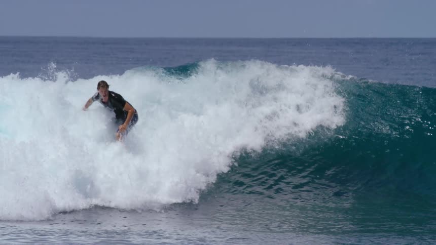 Male surfer with black t shirt and blue shorts rides on ocean wave