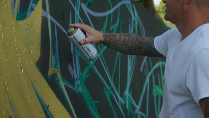 A man is using a can of spray paint to draw graffiti on a wall