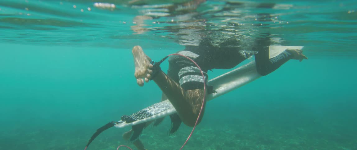 Woman sits on surfboardnear seafloor before paddling it out to sea