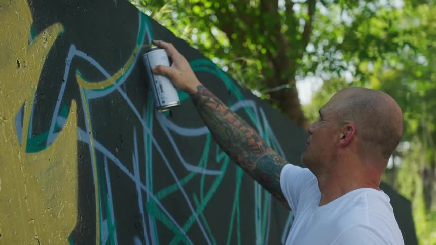 A man is spray painting a wall outdoors in spring