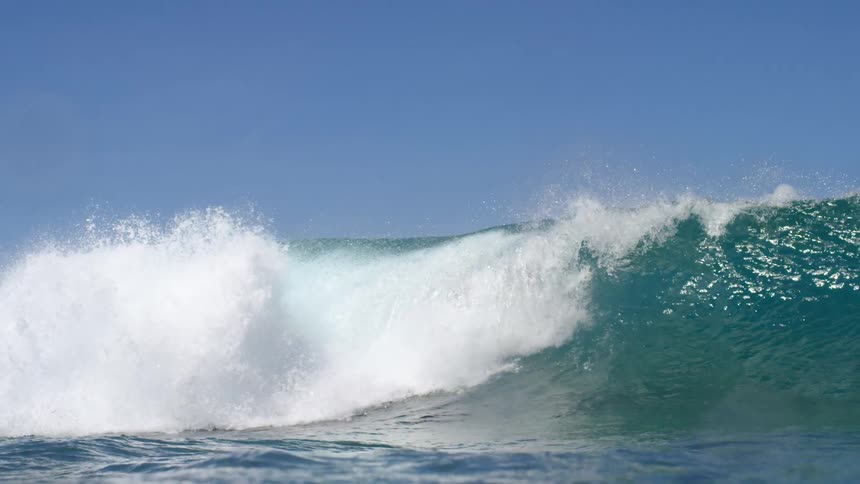 Young man surfing on an ocean wave under a blue sky