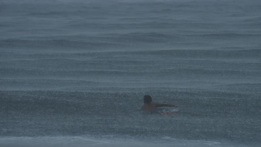 A surfer paddles out on his board while it rains