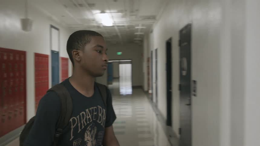 A boy walks over to a red locker and opens it