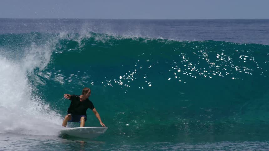 A teenage boy surfs over a large wave and then falls off his board