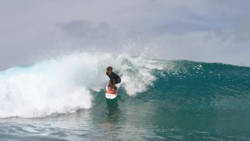 Male surfer with black t shirt and blue shorts rides on ocean wave