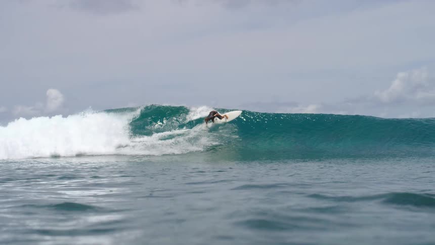 A surfer surfs in front of a large wave on the ocean during the day